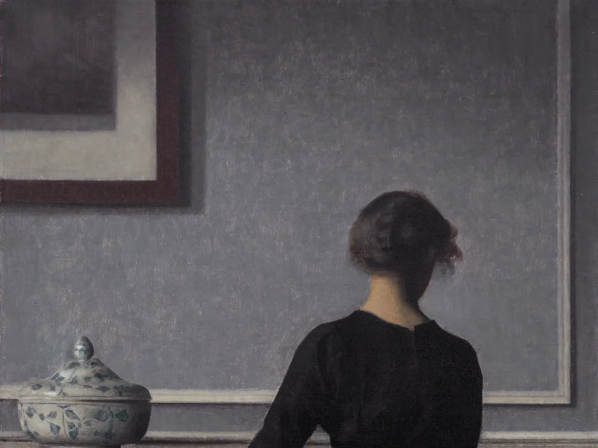 Vilhelm Hammershøi's interior: a woman seen from behind in a quiet grey room, morning light on the wall