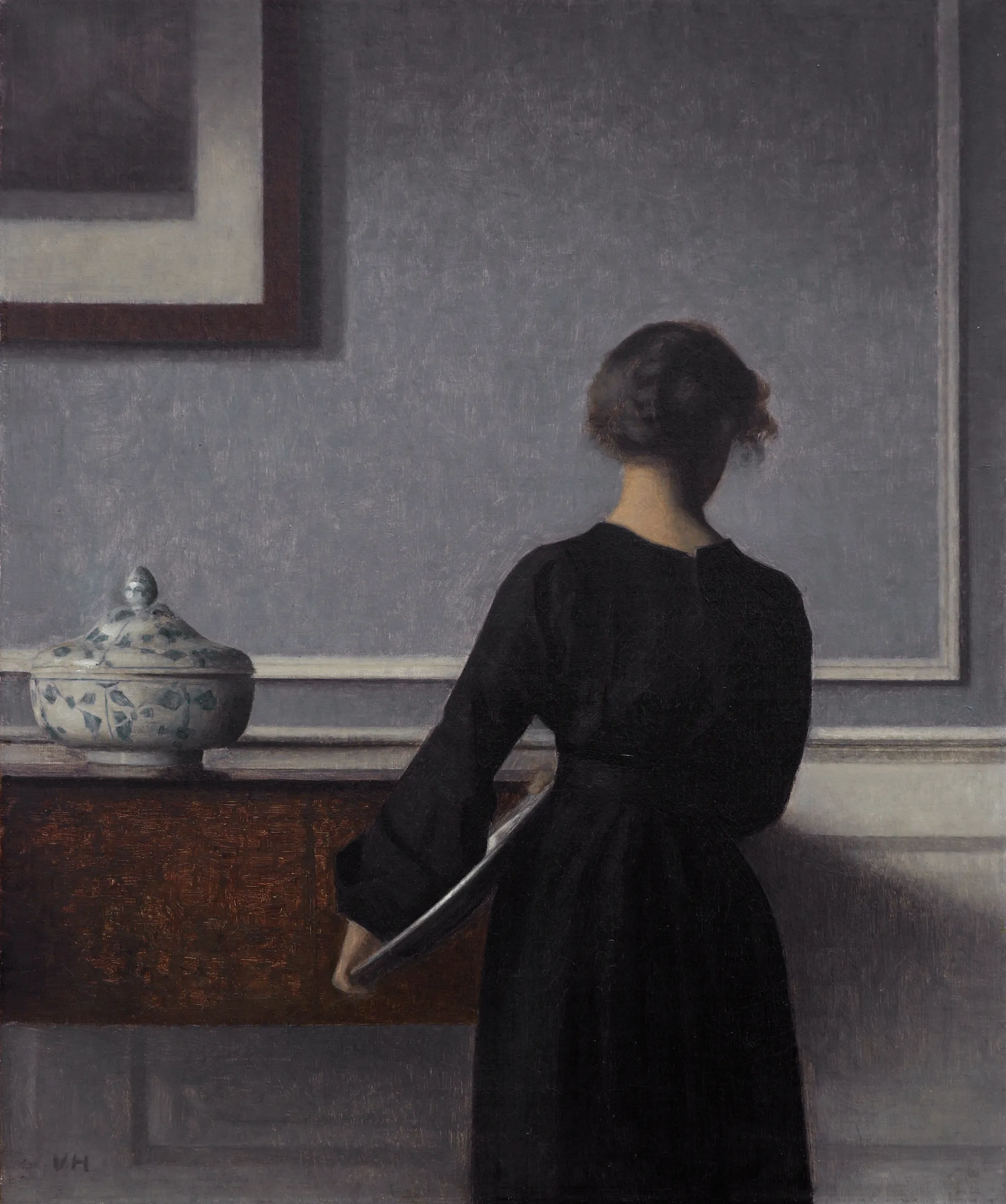 Vilhelm Hammershøi's interior: a woman seen from behind in a quiet grey room, morning light on the wall